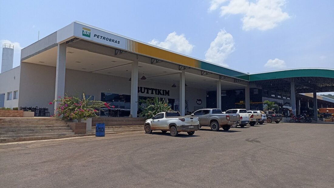 Posto de combustível à beira de rodovia no interior do Centro-Oeste, com caminhonetes estacionadas sob a cobertura