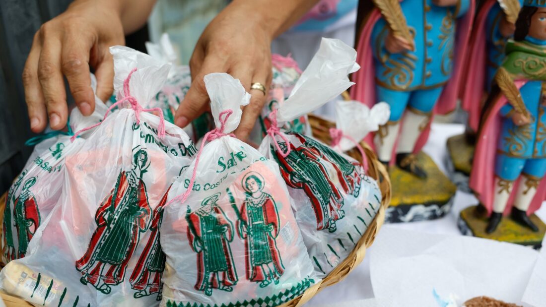 Mãos organizam saquinhos de doces estampados com a imagem de São Cosme e São Damião