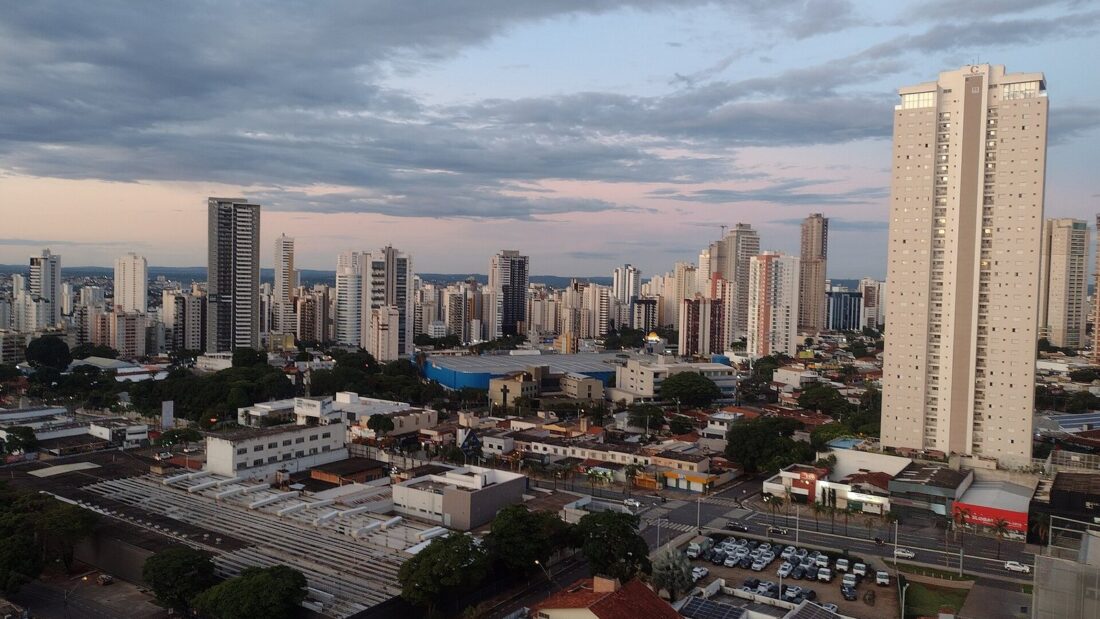 Vista de Goiânia com prédios altos ao fundo e casas e ruas em primeiro plano, sob céu nublado