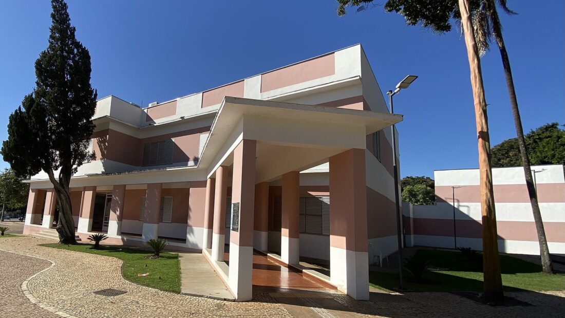 Fachada do Centro Cultural Marietta Telles Machado, prédio de dois pavimentos em tons de rosa e branco, com árvores e palmeira à frente, sob céu azul