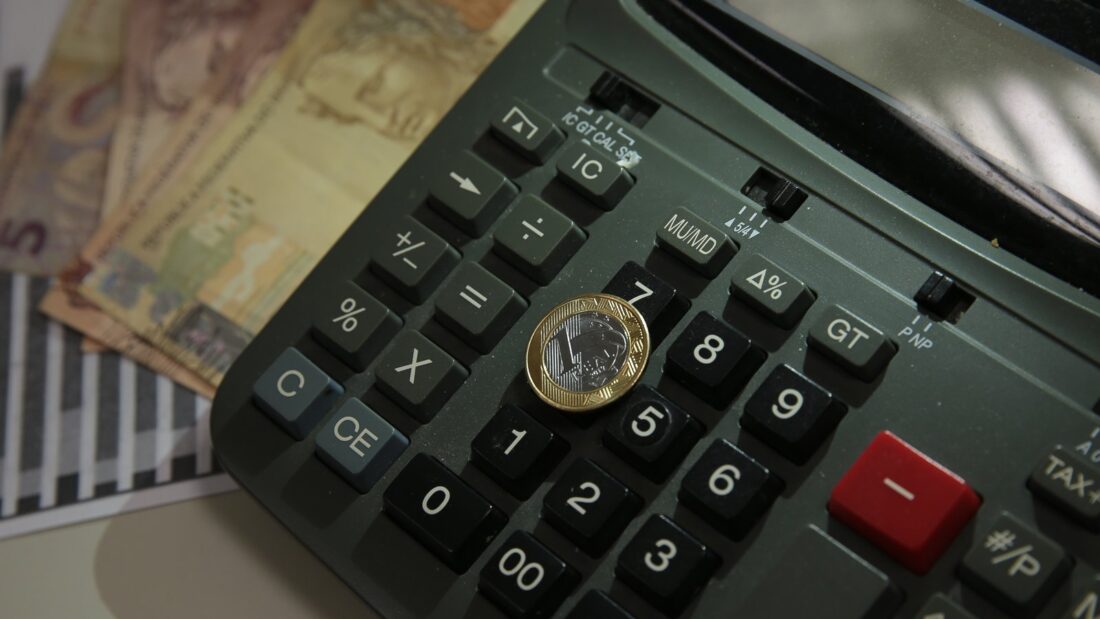 Calculadora, moeda e cédulas de real sobre a mesa