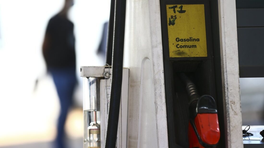 Bomba de gasolina comum em posto de combustível, com uma pessoa desfocada ao fundo