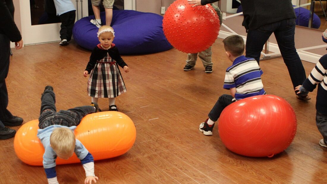 Crianças brincam com bolas de fisioterapia coloridas e almofadas grandes em uma sala de atividades sensoriais