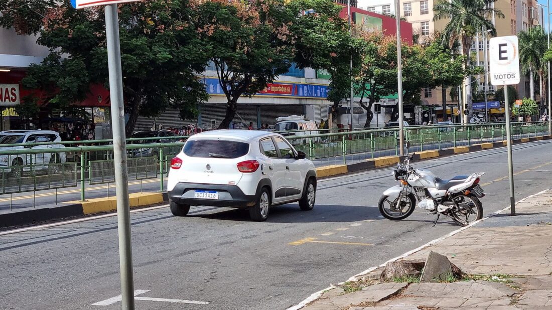 Avenida Anhanguera, no Centro de Goiânia, com carro e moto na pista, calçada e prédios ao fundo