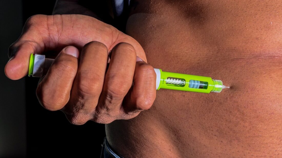 Pessoa aplica caneta injetável na região da barriga