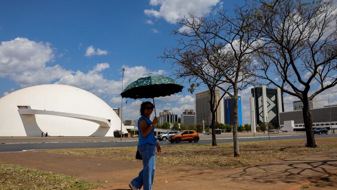 Mulher caminha com guarda-chuva para se proteger do sol perto do Museu Nacional, em Brasília
