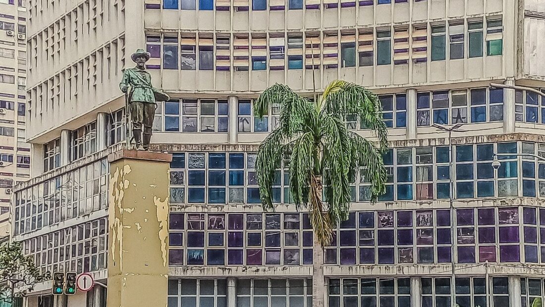 Avenida Goiás, no Centro de Goiânia, com prédio de fachada colorida, palmeiras e monumento