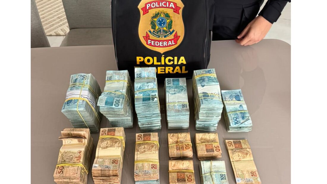 Maços de dinheiro sobre uma mesa ao lado de uma mochila da Polícia Federal
