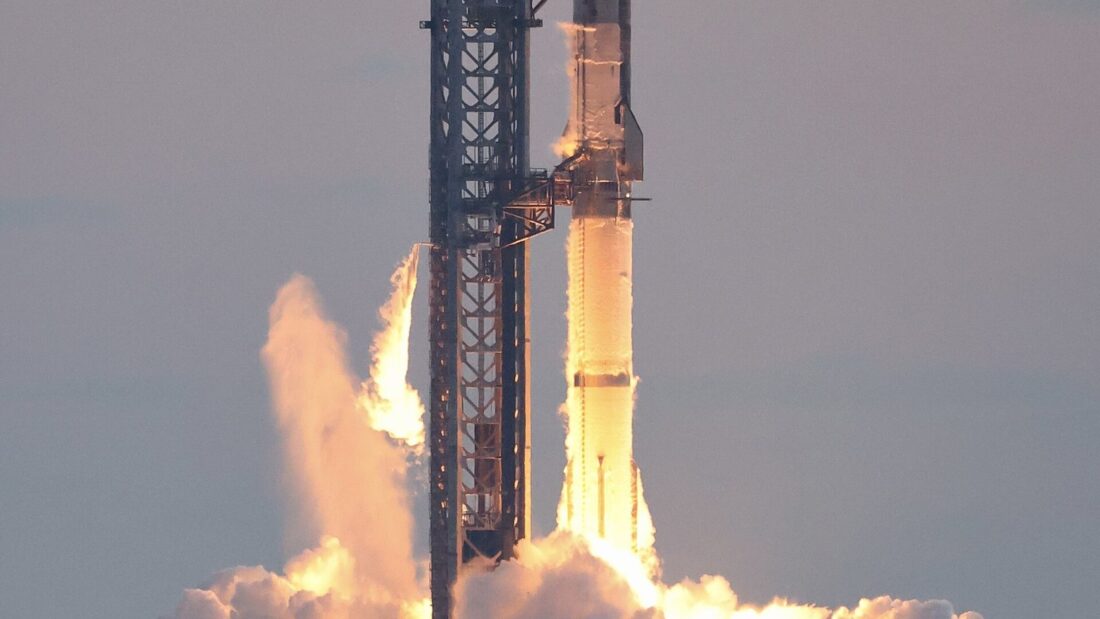 Foguete Starship decolando da base no Texas, com chamas e nuvem de fumaça ao lado da torre de lançamento