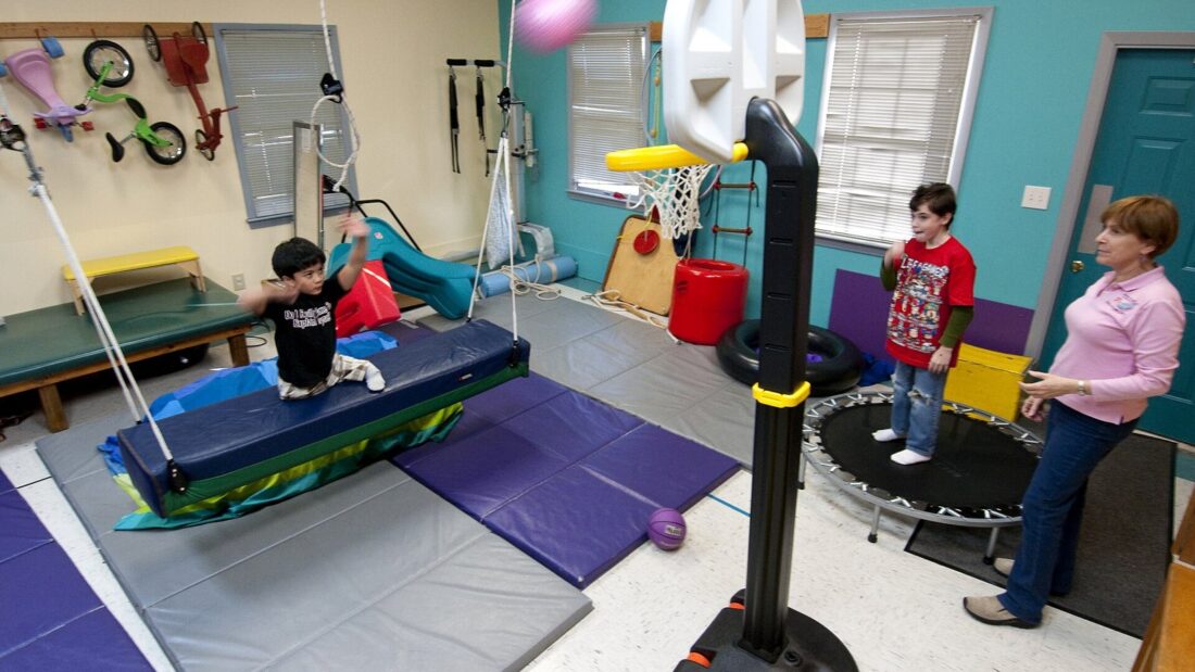 Sala de terapia ocupacional infantil com balanço suspenso, cama elástica, colchonetes e cesta de basquete