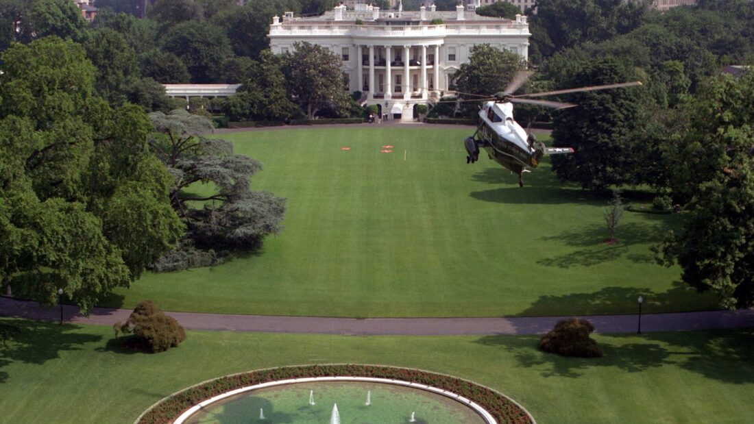 Vista aérea do gramado sul da Casa Branca, com um helicóptero pousado, a fonte circular e árvores ao redor