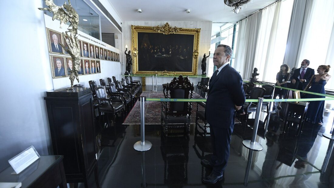O artista Vik Muniz, de terno escuro, observa o acervo de um salão histórico durante visita