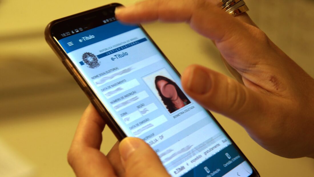 Mão segura celular com o aplicativo e-Título aberto na tela