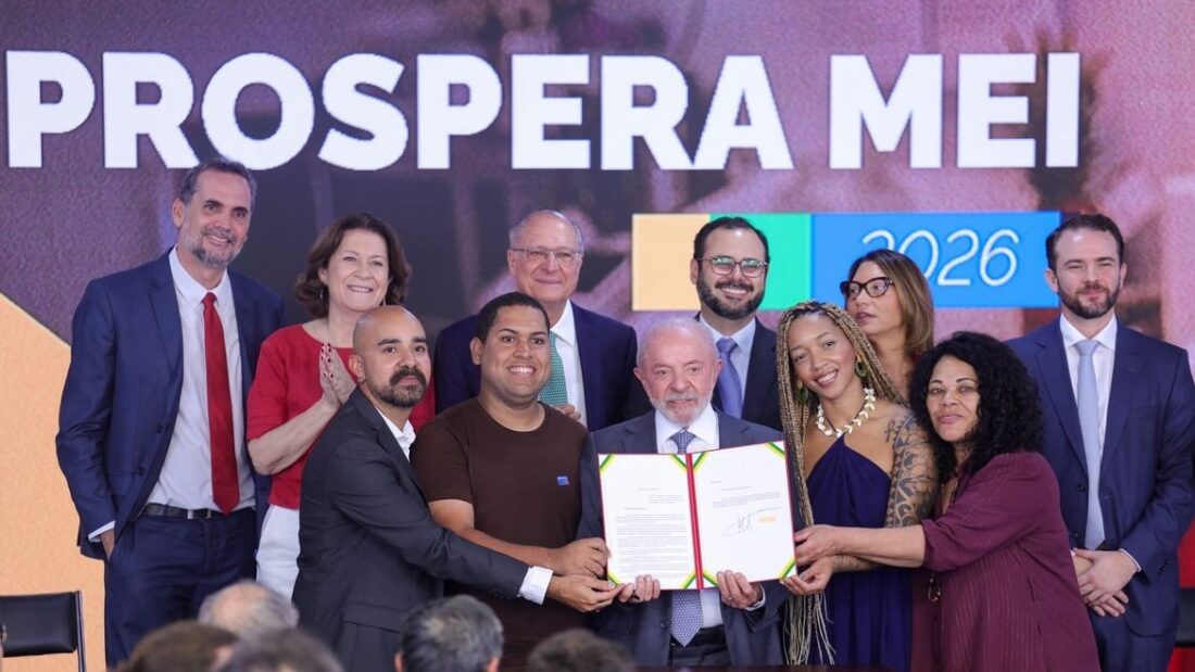 O presidente Lula, cercado por ministros e microempreendedores, segura um documento assinado diante de um painel com a inscrição Prospera MEI 2026