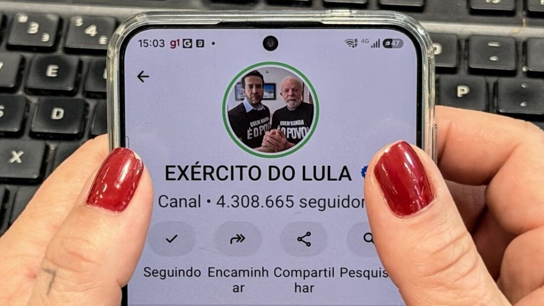 Mão de mulher com unhas vermelhas segurando um celular que mostra a página do canal de WhatsApp Exército do Lula