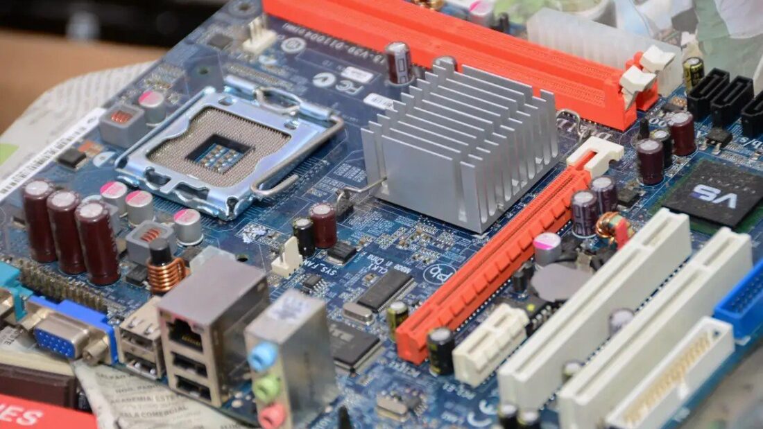 Placa-mãe de computador vista de perto, com processador, dissipador de calor prateado, capacitores e encaixes coloridos