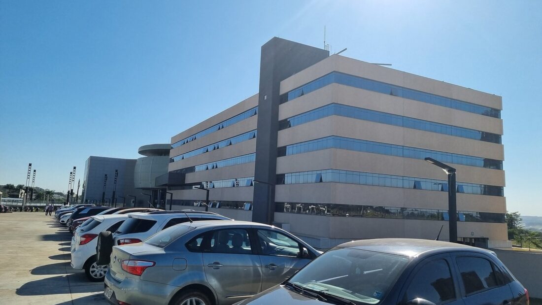 Prédio moderno de vários andares com fachada de vidro e concreto, sede da Assembleia Legislativa de Goiás, com carros estacionados à frente sob céu azul