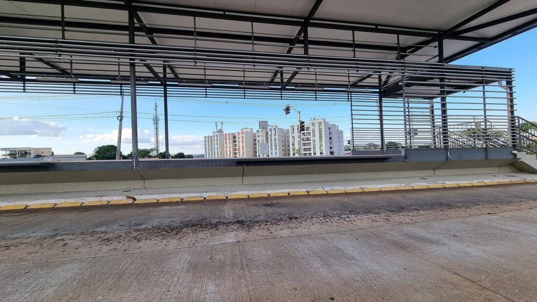 Plataforma vazia de uma estação do BRT Norte-Sul, com cobertura metálica e prédios residenciais ao fundo