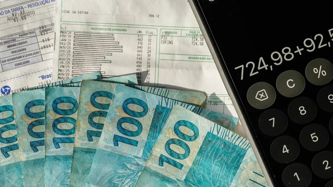 Notas de 100 reais ao lado de um celular com calculadora aberta e de um contracheque