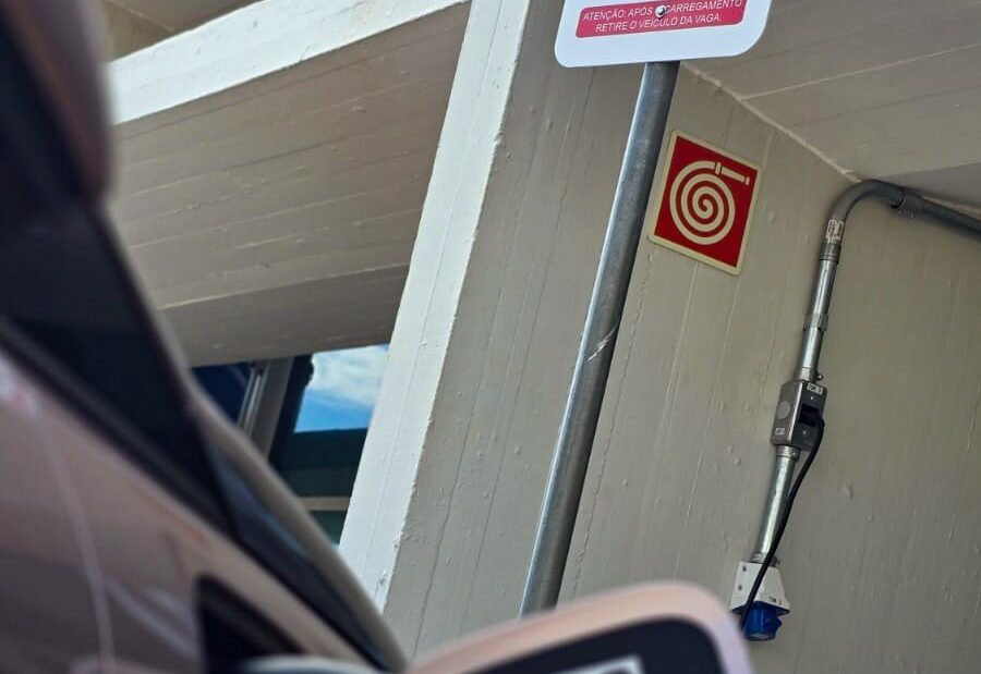 Carro elétrico conectado a um ponto de recarga em garagem, com placa indicando vaga para veículo elétrico