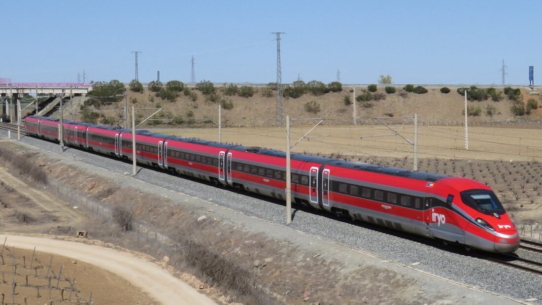 Trem vermelho de alta velocidade da empresa Iryo passa por linha férrea eletrificada em área de campo seco