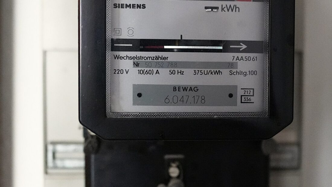 Medidor de energia elétrico antigo, de caixa preta, com o mostrador de quilowatts-hora e o disco giratório, preso a uma parede