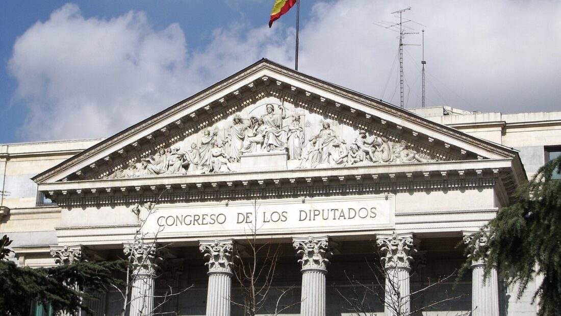 Fachada do Congresso dos Deputados, em Madri, com colunas, frontão esculpido e a bandeira da Espanha no alto do prédio