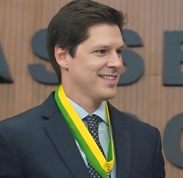 Daniel Vilela sorri, de terno, com uma medalha presa a uma fita verde e amarela