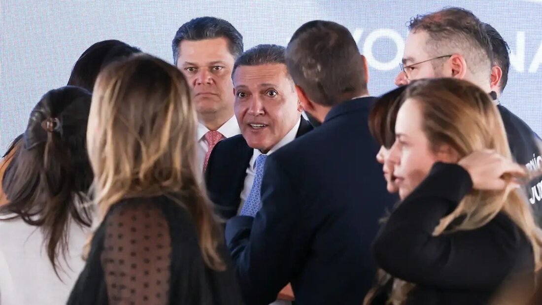 Ministro Kassio Nunes Marques cercado por autoridades e assessores em ambiente fechado, durante entrevista coletiva