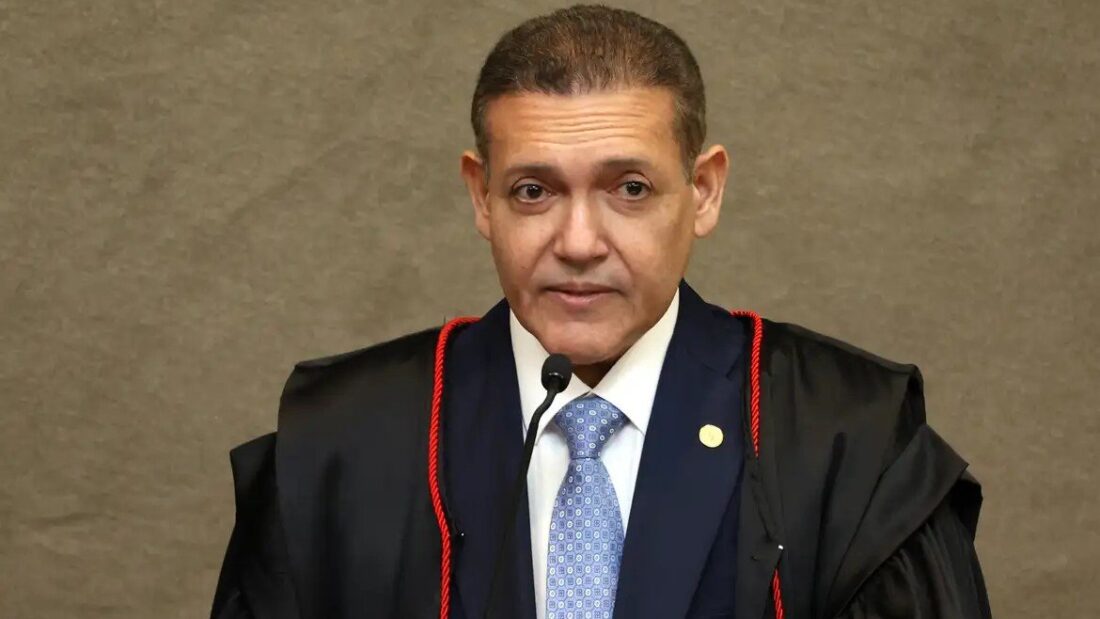 Ministro Kassio Nunes Marques, de toga preta e gravata azul, fala ao microfone diante de um painel de madeira