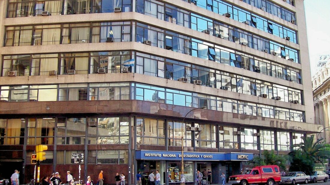 Prédio alto de escritórios com fachada de janelas em faixas horizontais, na esquina de uma avenida de Buenos Aires, com a placa do Instituto Nacional de Estadística y Censos na entrada