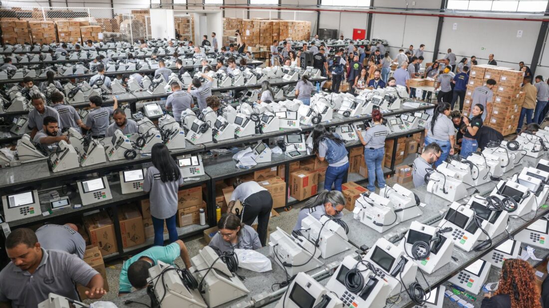 Servidores da Justiça Eleitoral preparam centenas de urnas eletrônicas enfileiradas em um galpão