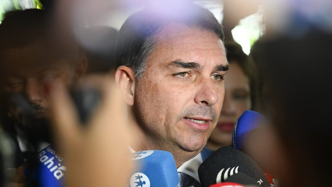 Flávio Bolsonaro fala cercado por microfones de emissoras durante entrevista