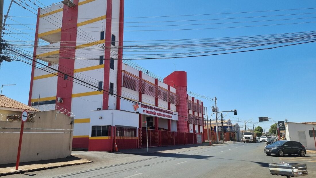 Prédio vermelho, amarelo e branco de um quartel do Corpo de Bombeiros, com torre de treinamento, visto de uma esquina