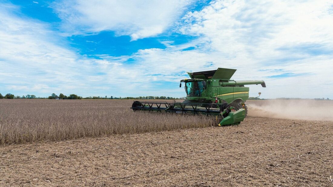Colheitadeira verde colhe soja em uma lavoura plana sob céu parcialmente nublado