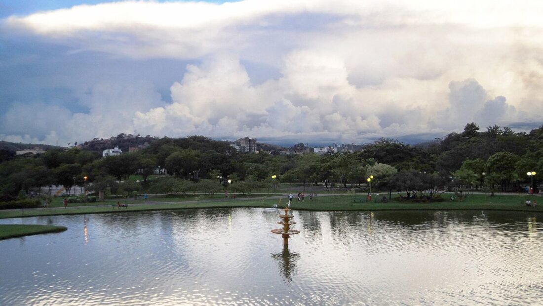 Nuvens de tempestade altas e carregadas se formam sobre um lago cercado de árvores, ao entardecer