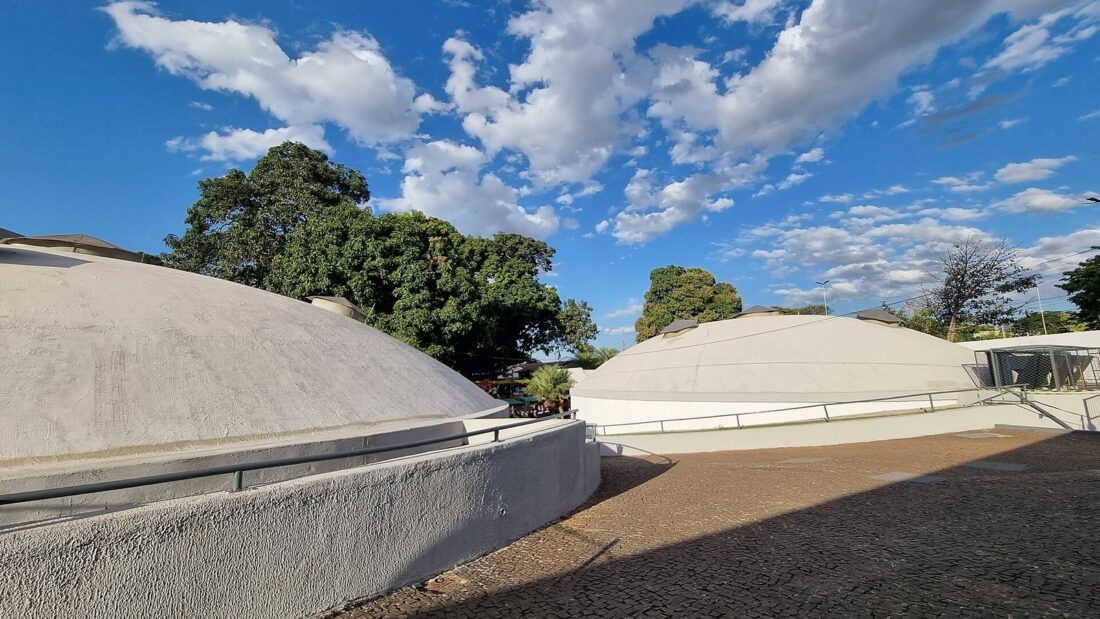 Pátio do Centro Cultural Martim Cererê, em Goiânia, com as duas construções em forma de cúpula branca e árvores ao fundo sob céu azul