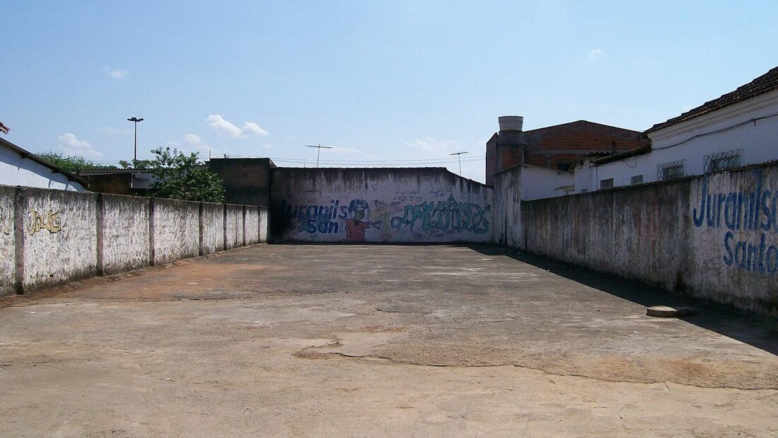Terreno vazio de chão de cimento cercado por muros pichados, com casas ao fundo, onde ficava a casa dos catadores que abriram a cápsula do Césio-137