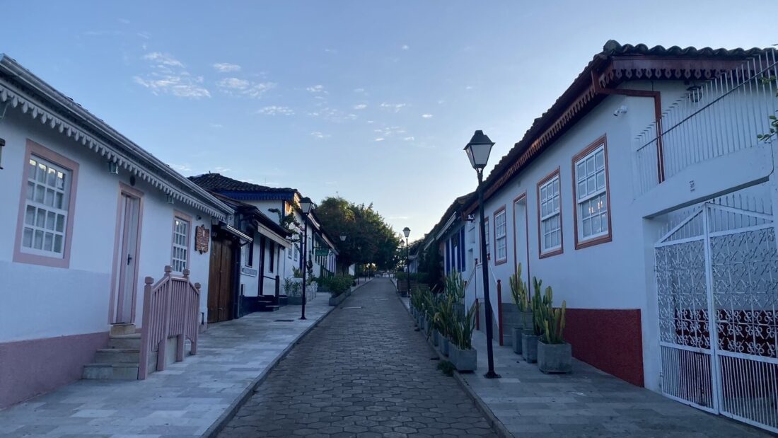 Rua de pedra no Centro Histórico de Pirenópolis, com casarões coloniais brancos de portas e janelas coloridas e um poste de luz antigo
