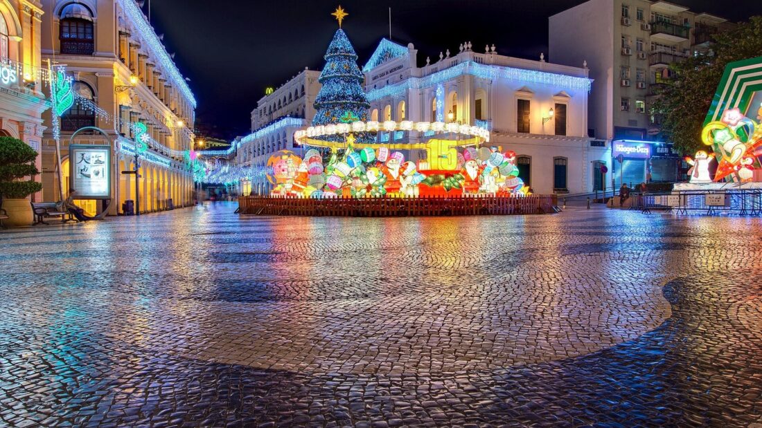 Largo do Senado, em Macau, à noite, com calçada de pedras portuguesas molhada, prédios coloniais iluminados e decoração de fim de ano
