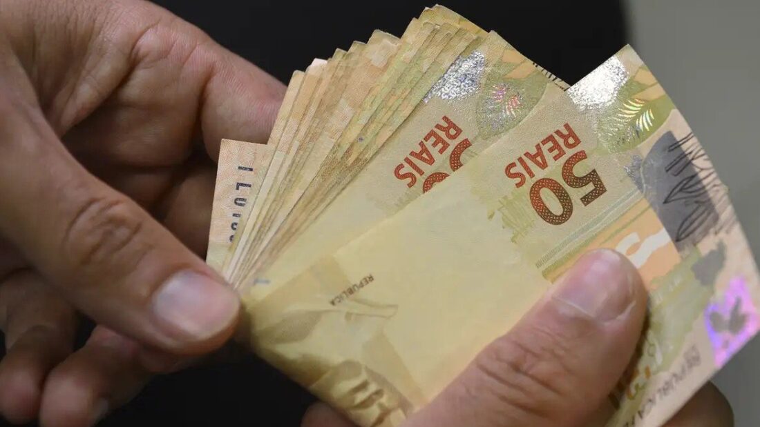 Mãos segurando um maço de cédulas de 50 reais