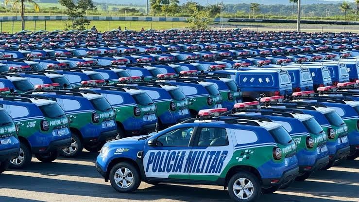 Pátio com dezenas de viaturas novas da Polícia Militar de Goiás, utilitários azuis com faixas verdes e brancas, estacionadas em fileiras