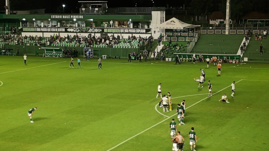Jogadores em campo durante partida noturna no Estádio Hailé Pinheiro, a Serrinha, com a arquibancada lotada de torcedores do Goiás