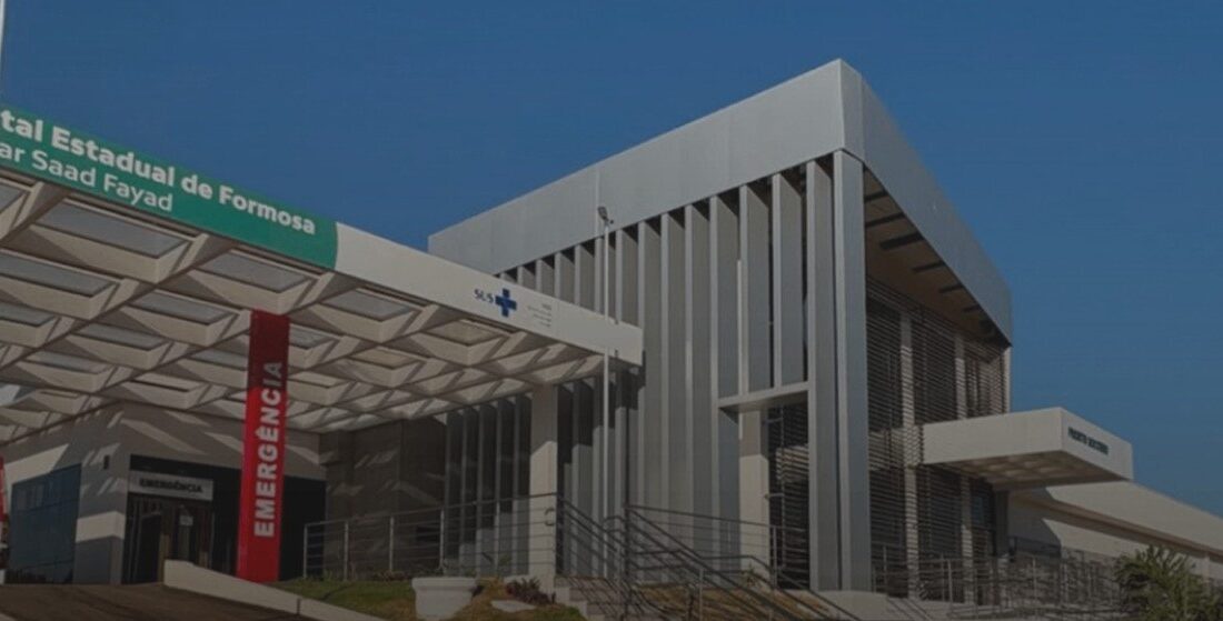 Fachada moderna e branca do Hospital Estadual de Formosa Dr. César Saad Fayad, com letreiro verde, cobertura na entrada e ambulância estacionada