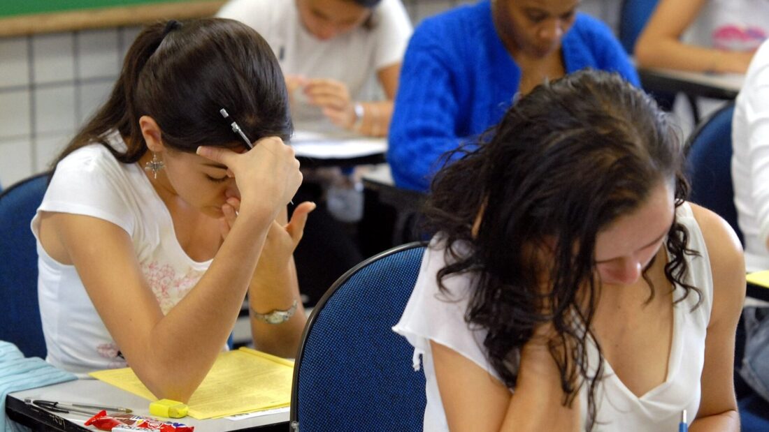 Estudantes sentados em carteiras escolares fazem prova em uma sala de aula