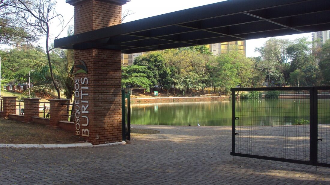 Portal de entrada do Bosque dos Buritis, em Goiânia, com pilar de tijolos, lago e árvores ao fundo