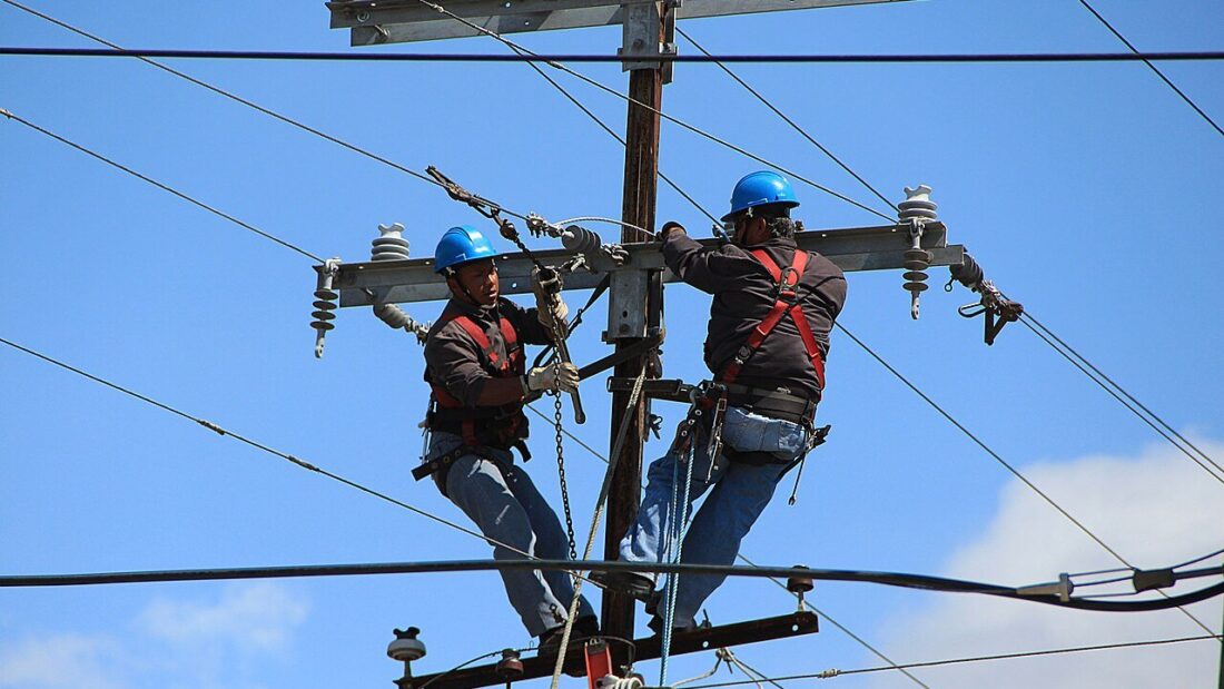 Dois eletricistas trabalham no alto de um poste da rede elétrica