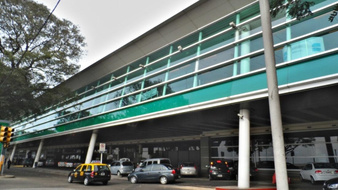 Fachada envidraçada do terminal de passageiros do Aeroparque Jorge Newbery, em Buenos Aires, com carros e táxis na pista de acesso