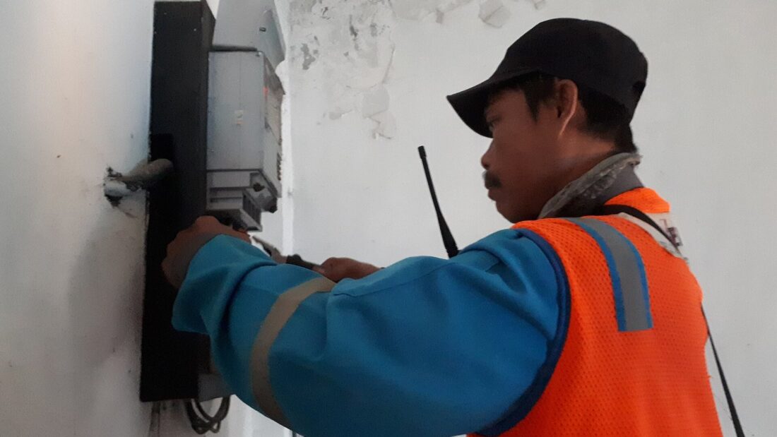 Eletricista de boné e colete laranja mexe num medidor de energia instalado numa parede