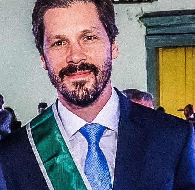 Daniel Vilela, homem de barba, terno azul, gravata azul clara e faixa verde de condecoração atravessada no peito, sorrindo